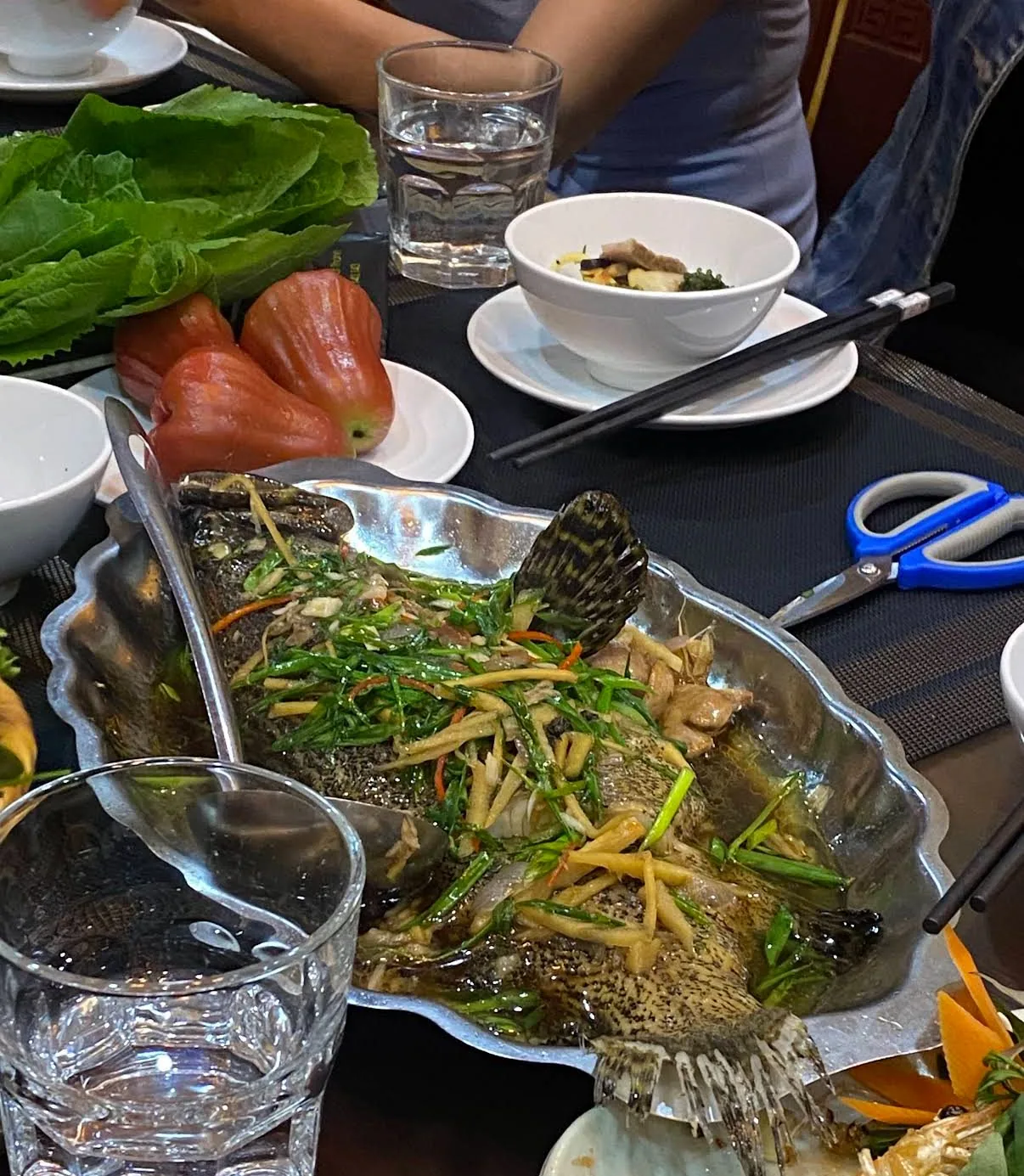 Cá hấp nguyên con với gừng và rau xanh tại bàn ăn